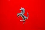 Close-up of a luxury car emblem on a glossy red surface displaying elegance and style.